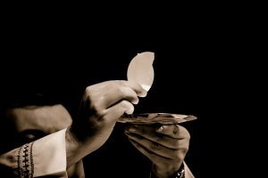 priest's hands holding communion up over a plate.