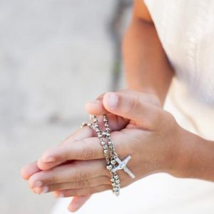 Detail of a girls hands holding rosary beads with crucifix during first holy communion.