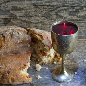 Broken bread and a chalice of red wide, communion wine, on a rustic, wooden table.