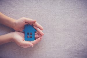 Hands holding a blue, paper cut out of a house.