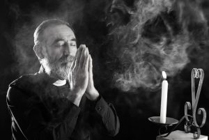 Black and white photo of a priest praying next to a candle.