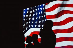 Silhouettes of people standing in front of the American flag.
