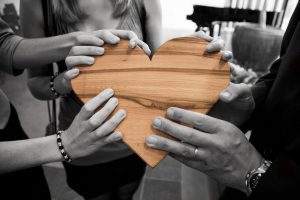 Four set of hands holding a wooden heart