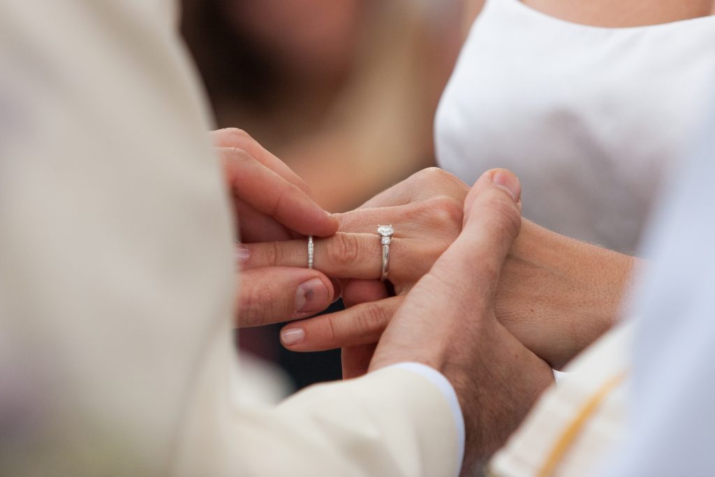 Groom sliding wedding ring onto bride's finger